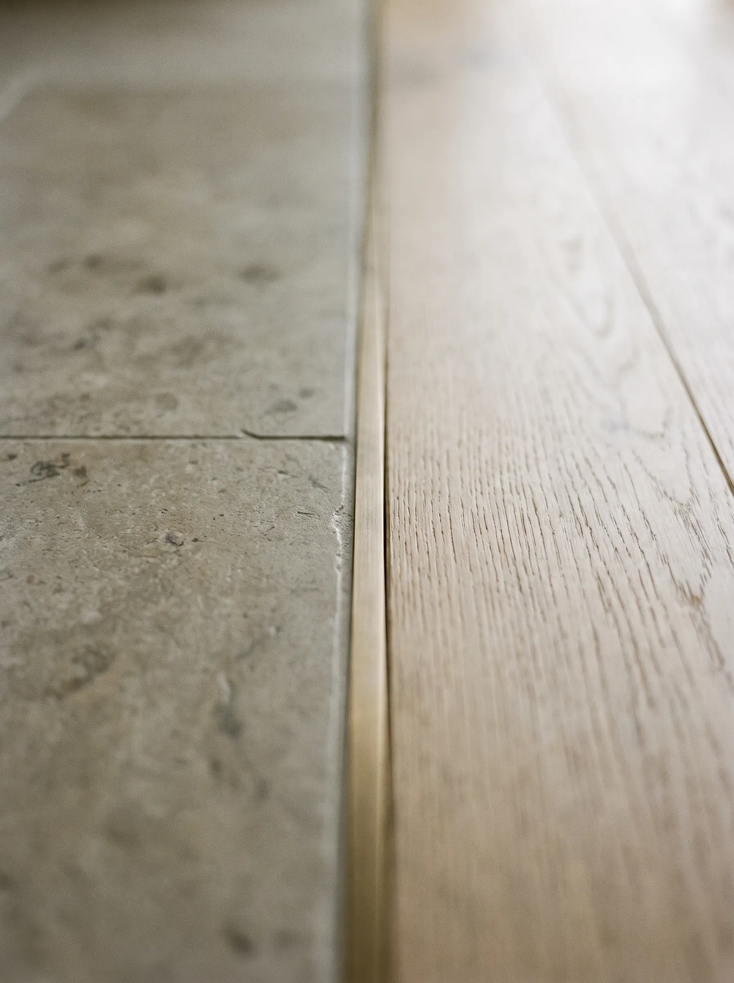 Flush metal transition where limestone tile meets an oak floor